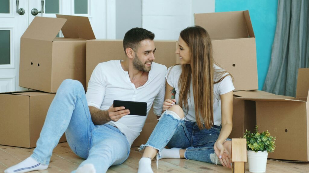 Un couple discute dans un appartement, assis devant une pile de cartons de déménagement