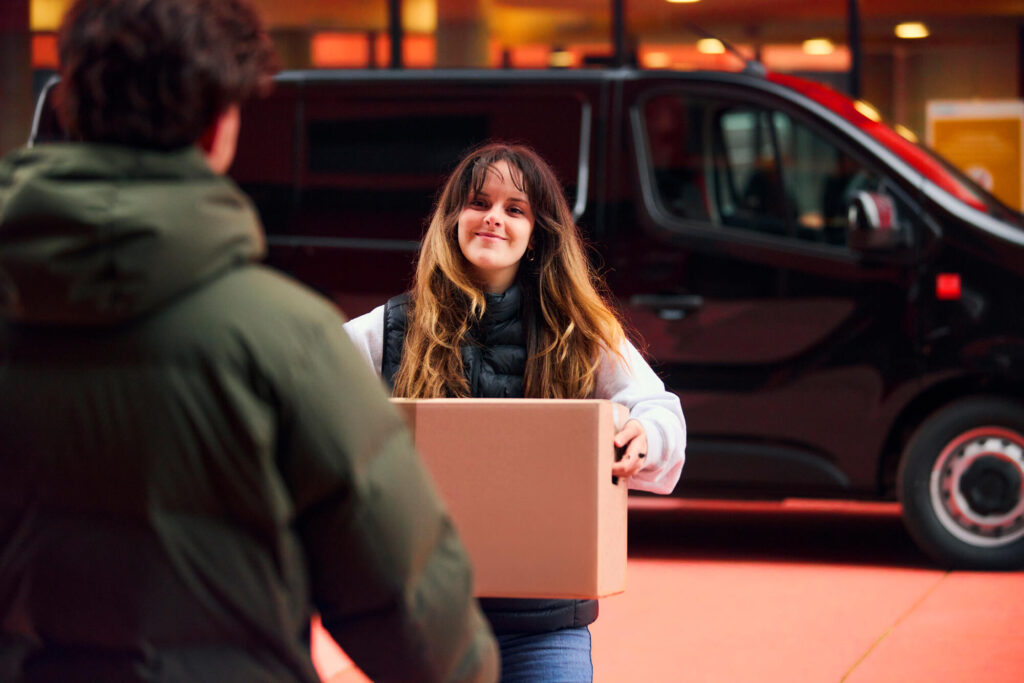 Femme remet un colis à un client devant van