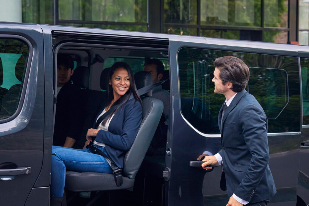 Femme souriante dans van avec chauffeur ouvrant porte